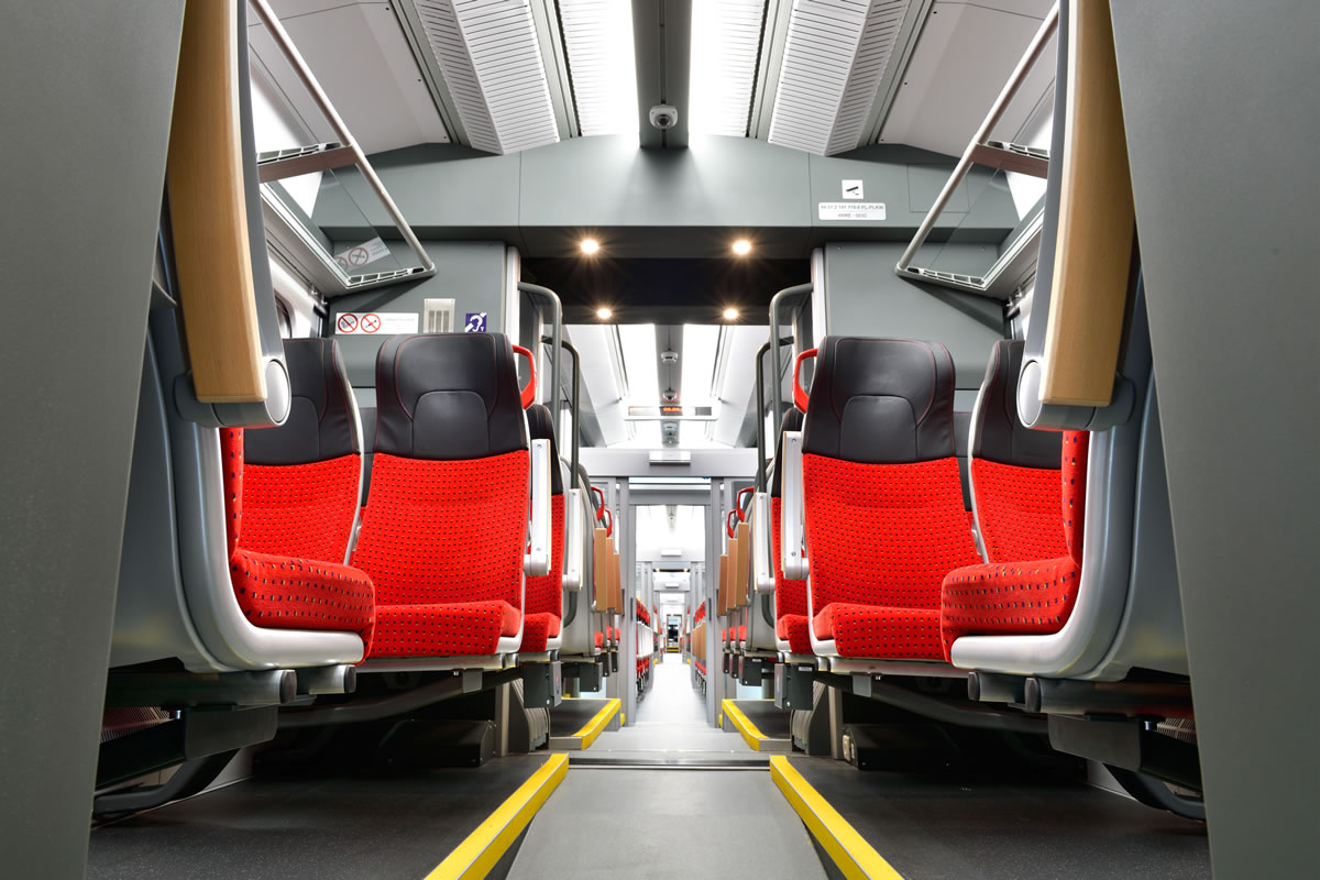 Rail carriage interior with red and black passenger seats either side of the aisle